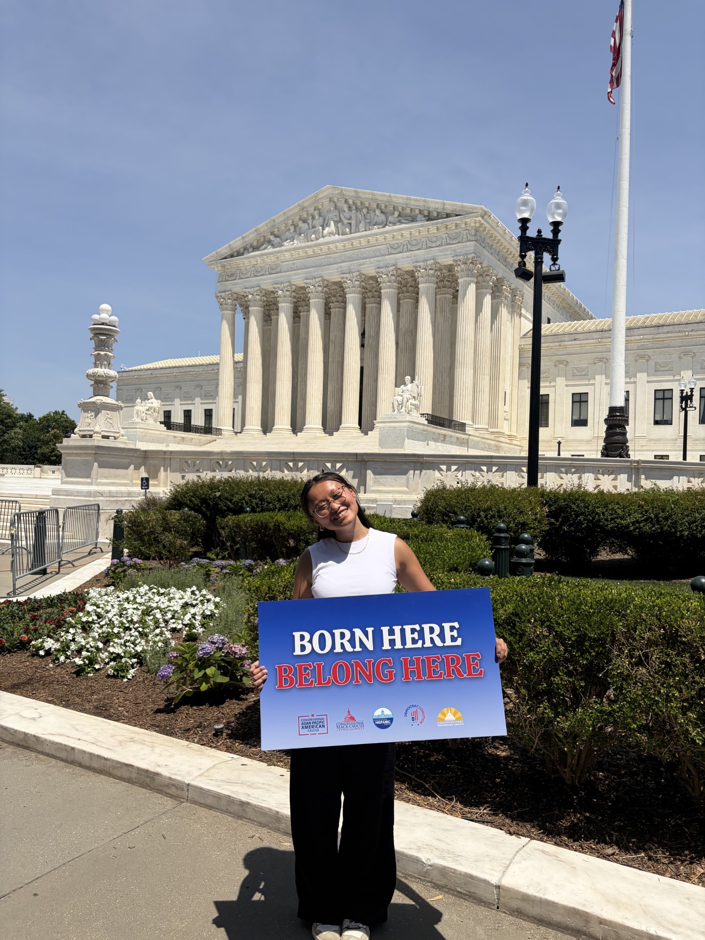 Grace Herzog in front of the Supreme Court with a sign reading "Born Here, Belong Here"